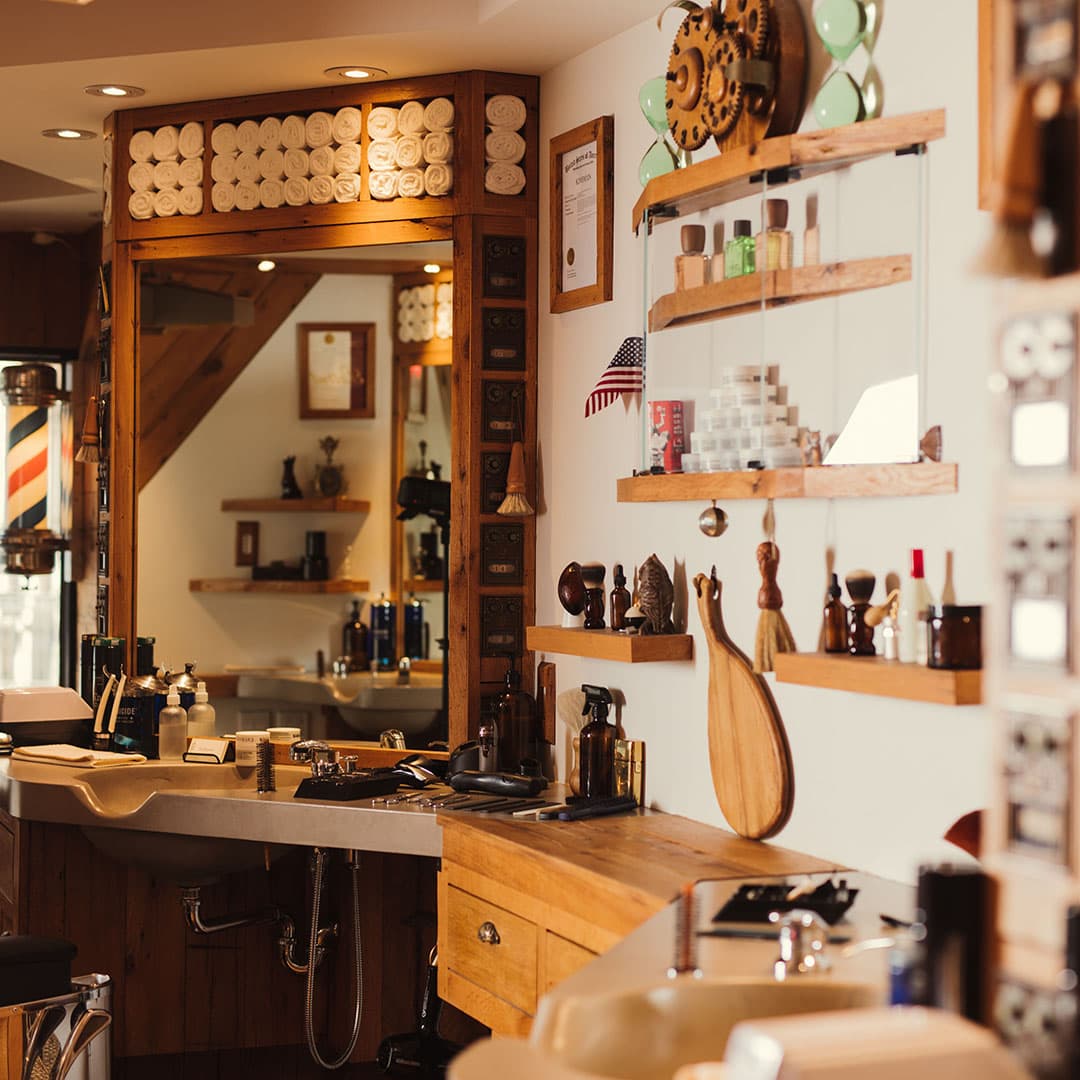 Wide-angle shot of The Kinsman barbershop's interior, showcasing antique wooden stations, folded towels, and a vintage barber pole, embodying West Village charm.