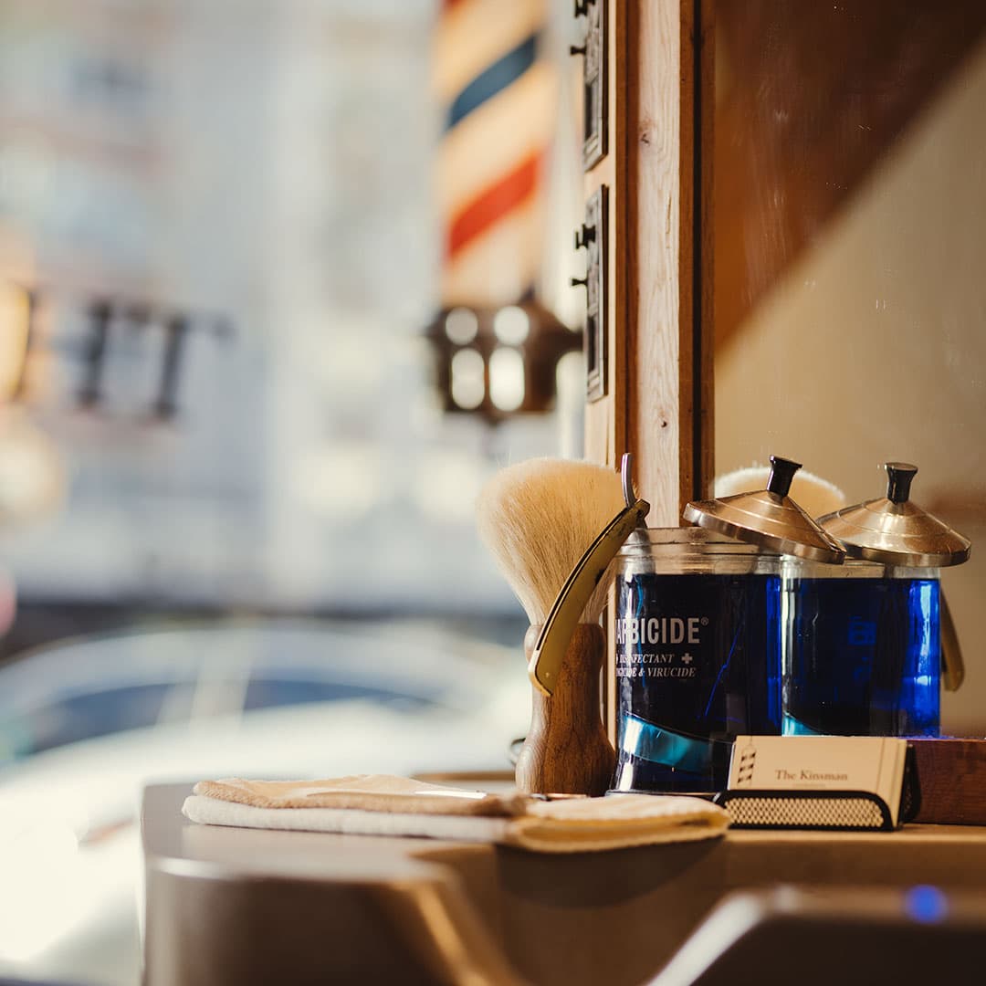 Professional grooming tools including Barbicide disinfectant jars, a shaving brush, and a straight razor at a West Village barber station.
