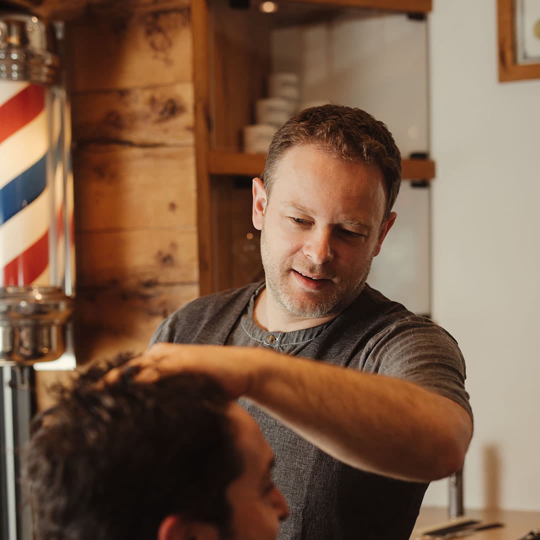 A skilled barber carefully styling a client's hair by hand, demonstrating the personalized attention and modern craft at The Kinsman shop.