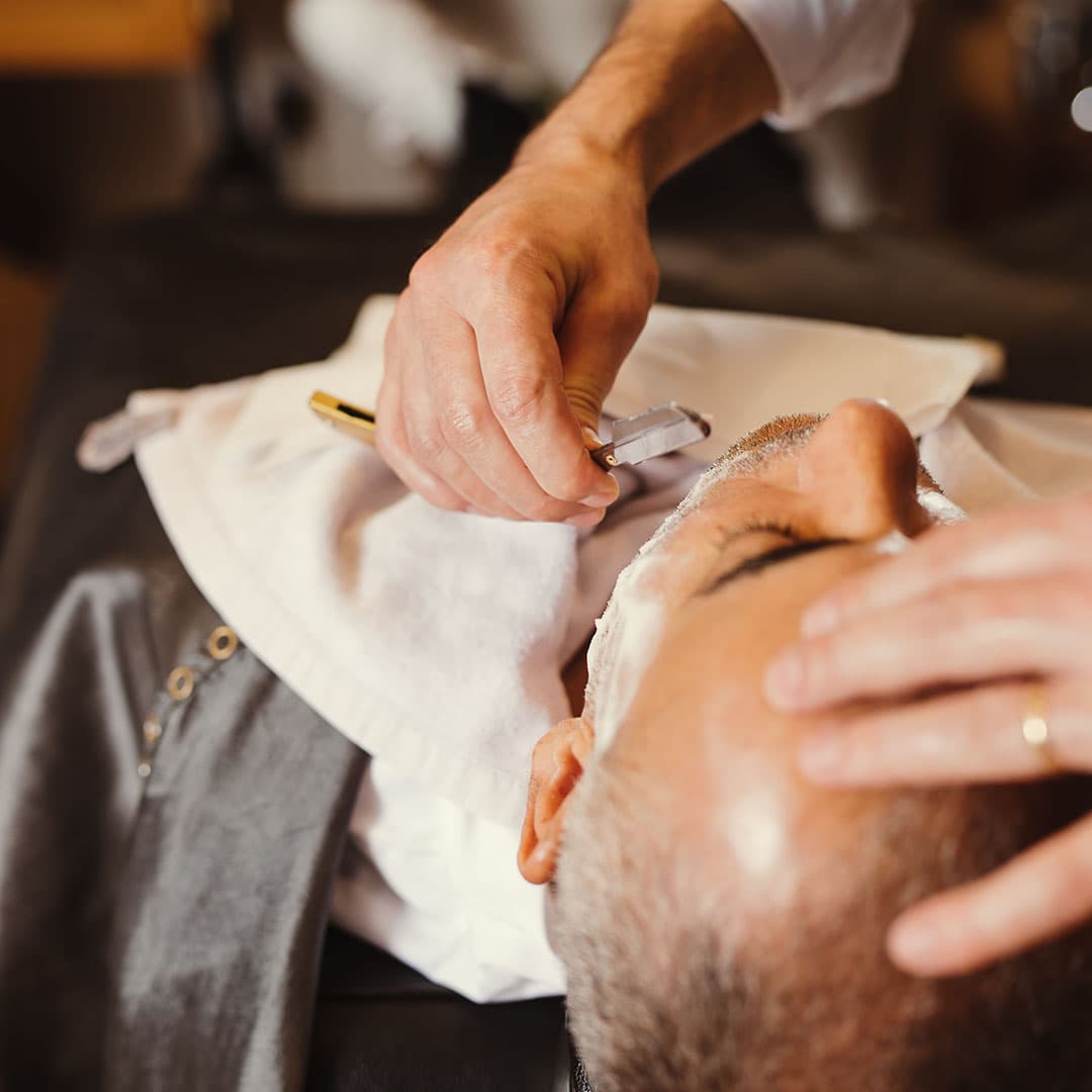 A master barber performing a precision straight razor shave on a client at The Kinsman, focusing on traditional hot towel grooming techniques.