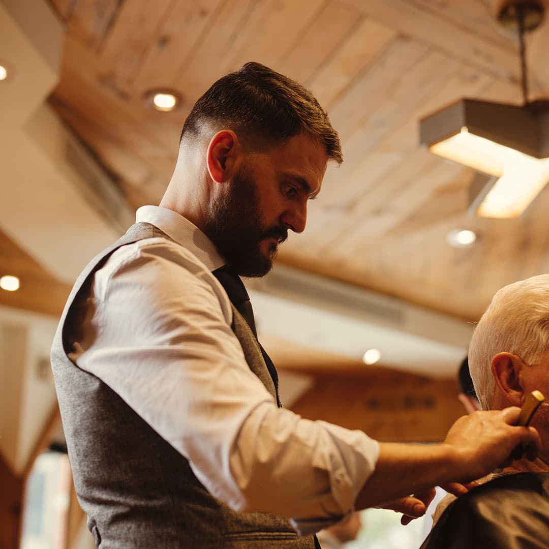 Action shot of a master barber finishing a classic men's haircut with precise scissors, showing the craftsmanship at The Kinsman in Manhattan.