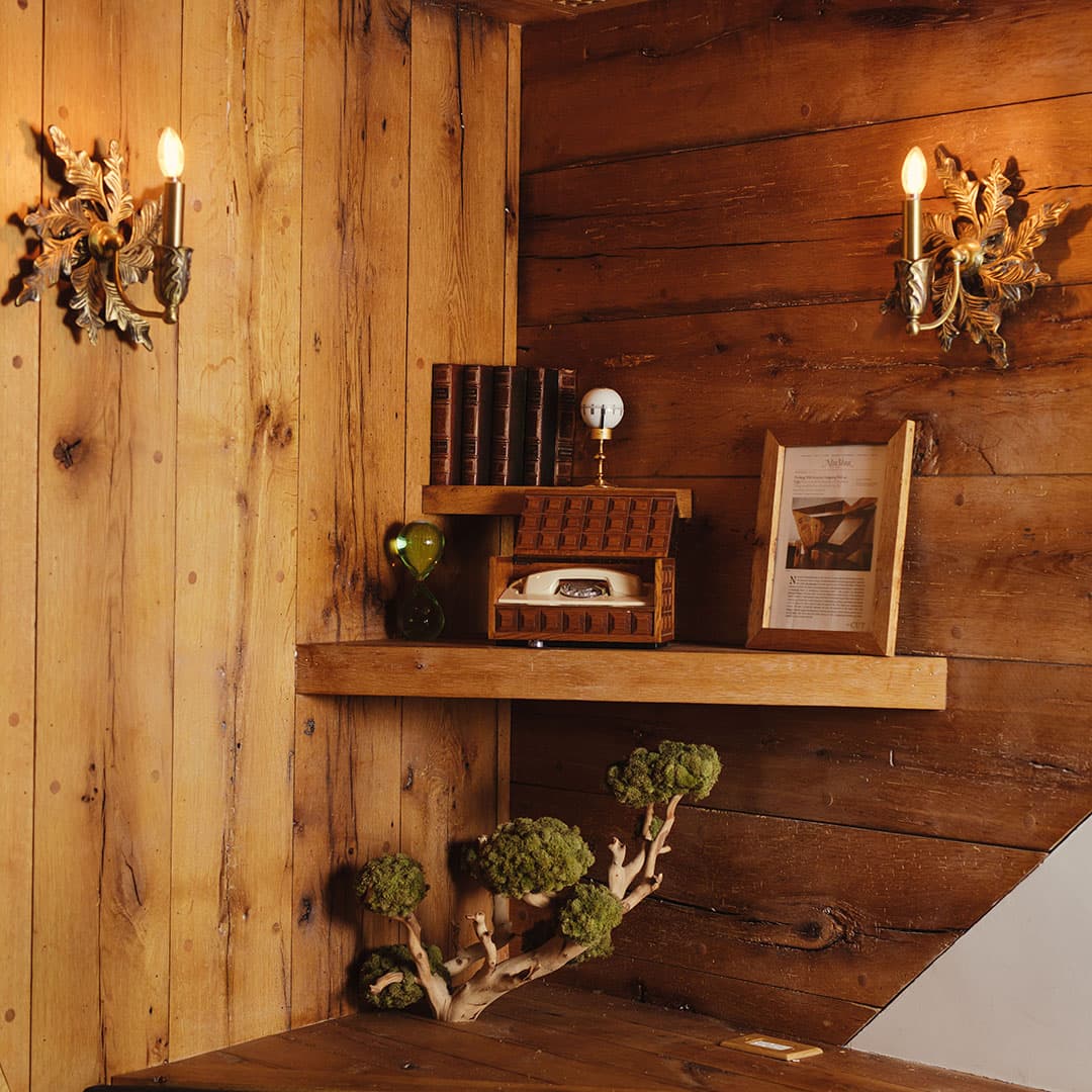 Interior decor of a luxury Manhattan barbershop featuring rustic wood paneling, vintage lighting fixtures, and a classic rotary telephone on a shelf.