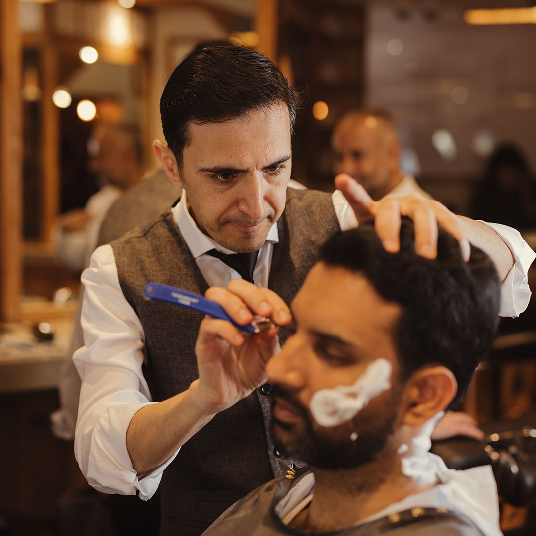 A barber using a straight razor for a traditional hot towel shave.